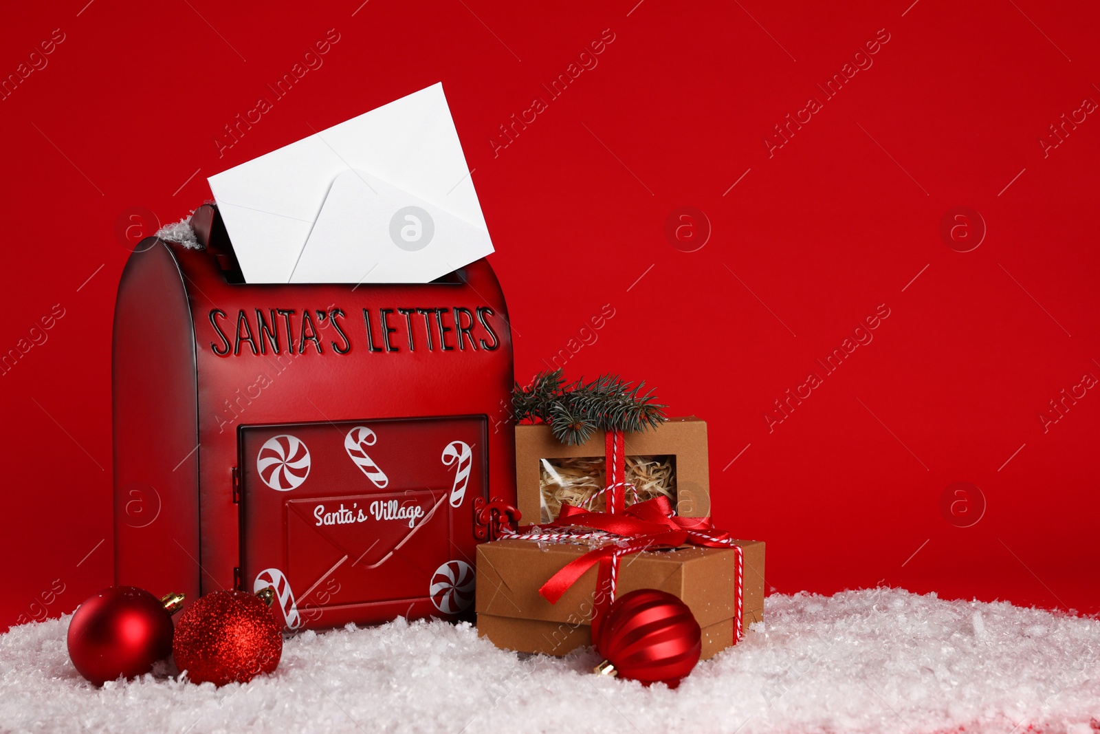 Photo of Santa Claus mailbox with envelope, fir tree branch, Christmas gifts, baubles and artificial snow on red background, space for text