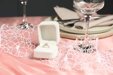 Engagement ring in box and tableware on pink tablecloth, closeup. Romantic dinner