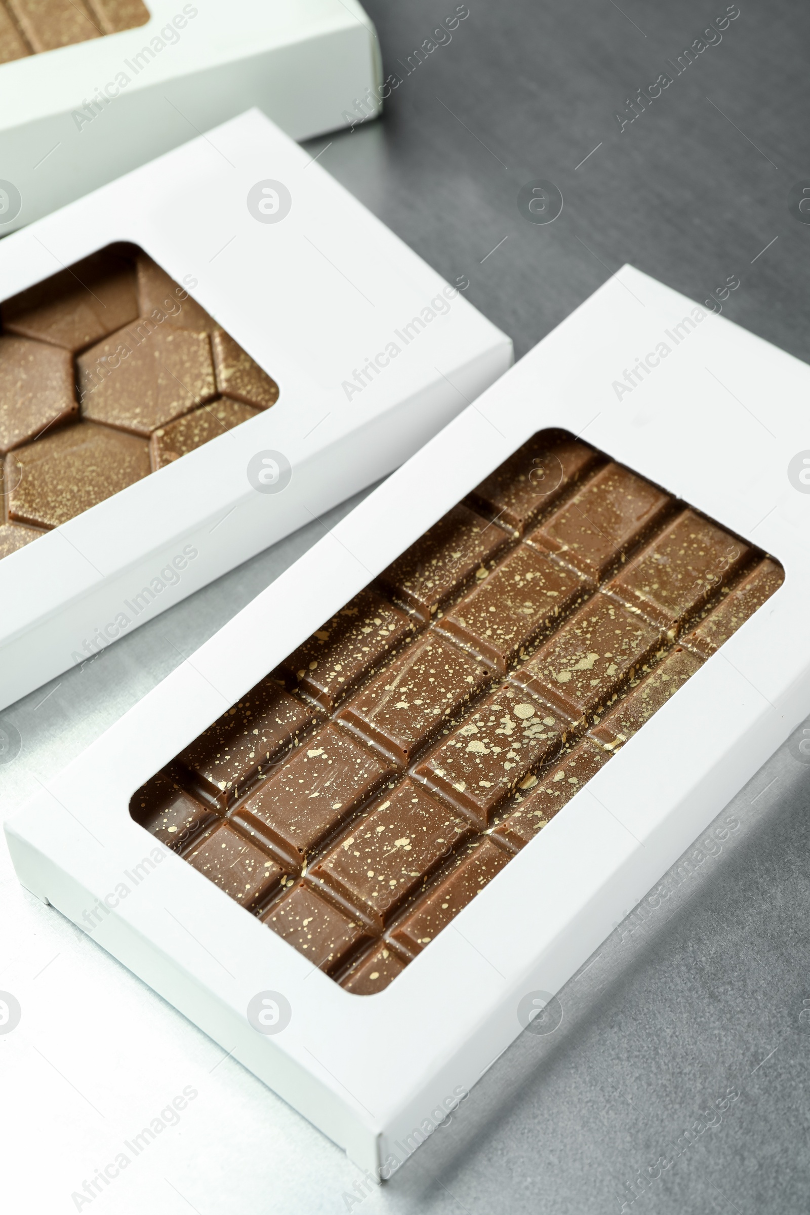 Photo of Different tasty Dubai chocolate bars in packages with pistachios and knafeh on grey table, closeup. Space for text