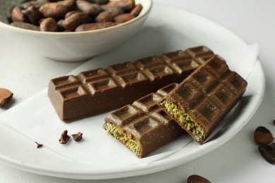 Photo of Tasty Dubai chocolate bars with pistachios, knafeh and cocoa beans on light table, closeup