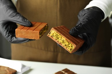 Photo of Woman holding pieces of tasty Dubai chocolate with pistachios and knafeh at white table, closeup