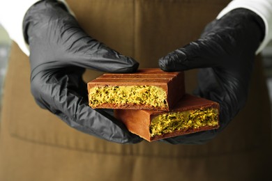 Photo of Woman holding pieces of tasty Dubai chocolate with pistachios and knafeh, closeup