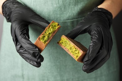 Photo of Woman holding pieces of tasty Dubai chocolate with pistachios and knafeh, closeup