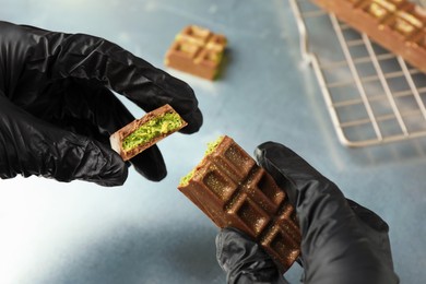 Photo of Woman holding pieces of tasty Dubai chocolate with pistachios and knafeh at grey table, closeup