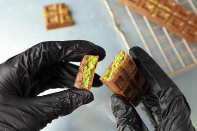 Photo of Woman holding pieces of tasty Dubai chocolate with pistachios and knafeh at grey table, closeup