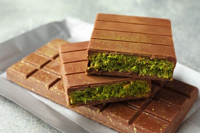 Photo of Tasty Dubai chocolate with pistachios and knafeh on grey textured table, closeup