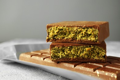 Photo of Tasty Dubai chocolate with pistachios and knafeh on grey textured table, closeup