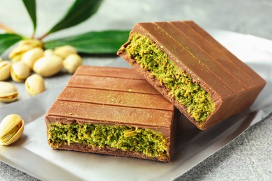 Photo of Pieces of tasty Dubai chocolate with pistachios and knafeh on grey textured table, closeup