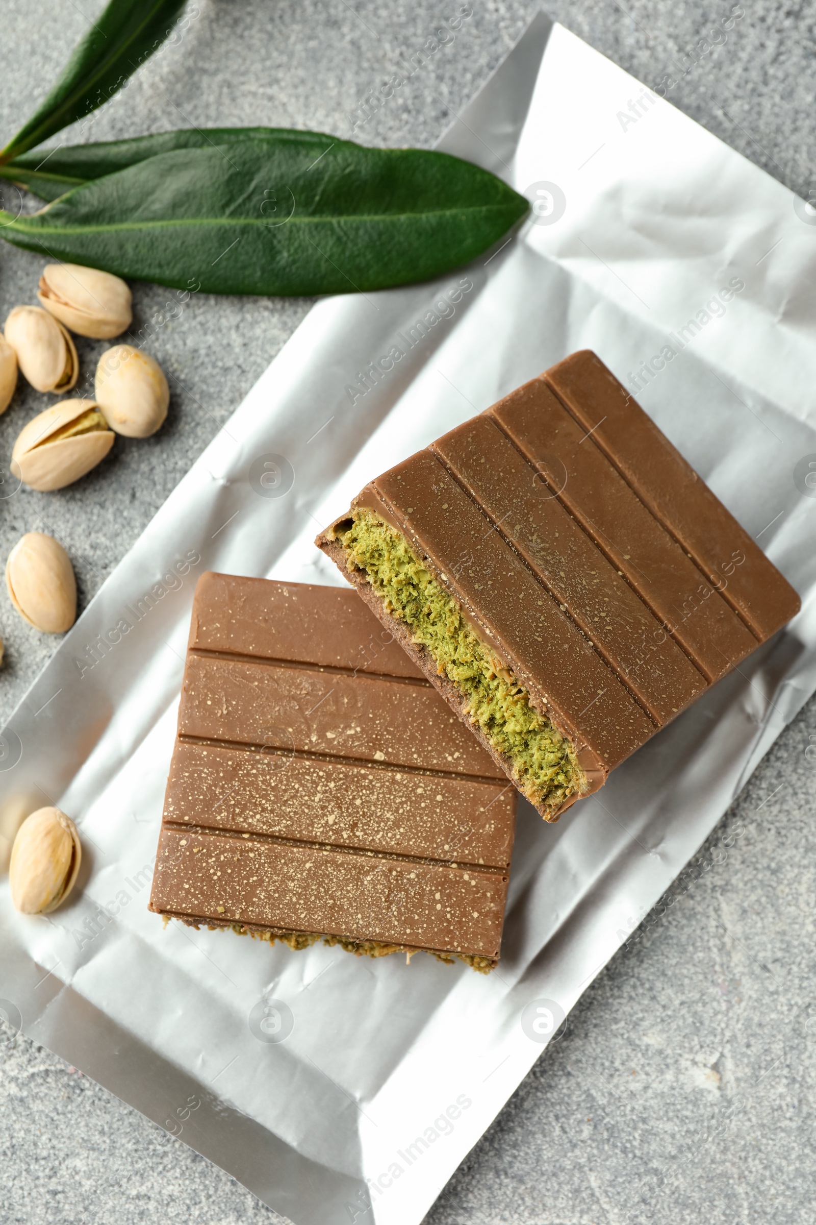 Photo of Pieces of tasty Dubai with pistachios and knafeh on grey textured table, flat lay