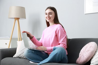 Photo of Smiling young woman with laptop on sofa at home