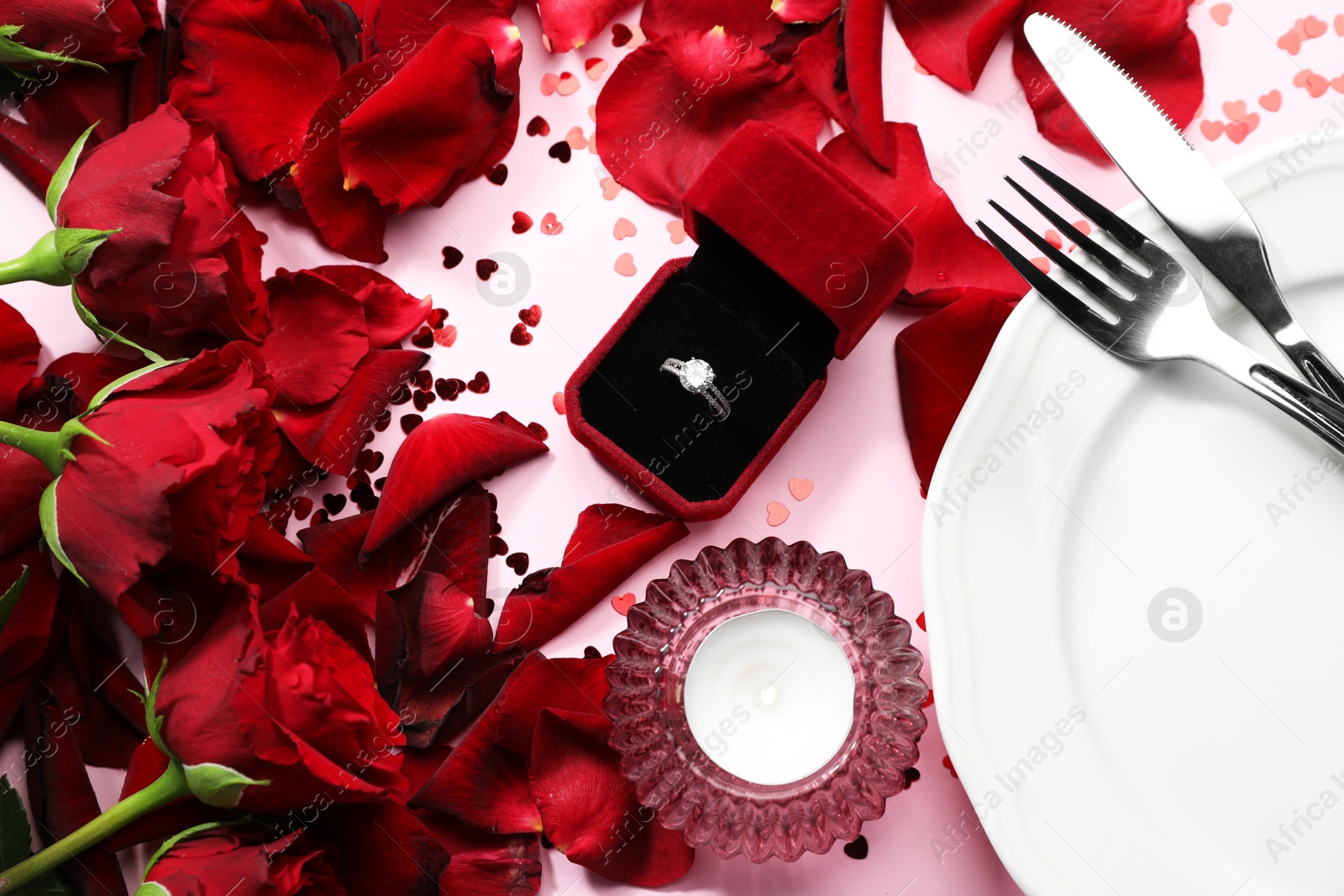 Photo of Beautiful setting for romantic dinner, engagement ring and roses on light pink table, flat lay