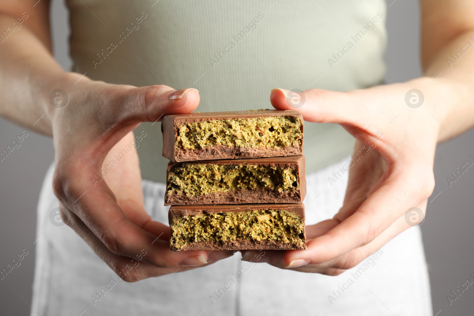 Photo of Woman holding pieces of delicious Dubai chocolate with pistachios and knafeh on grey background, closeup