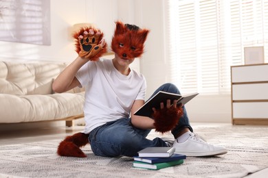 Photo of Quadrobics. Boy in fox mask, gloves and tail reading book at home