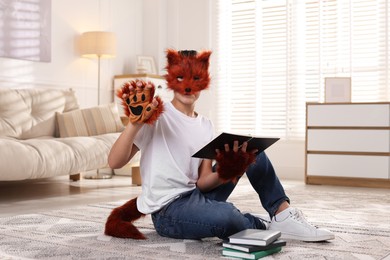 Photo of Quadrobics. Boy in fox mask, gloves and tail reading book at home