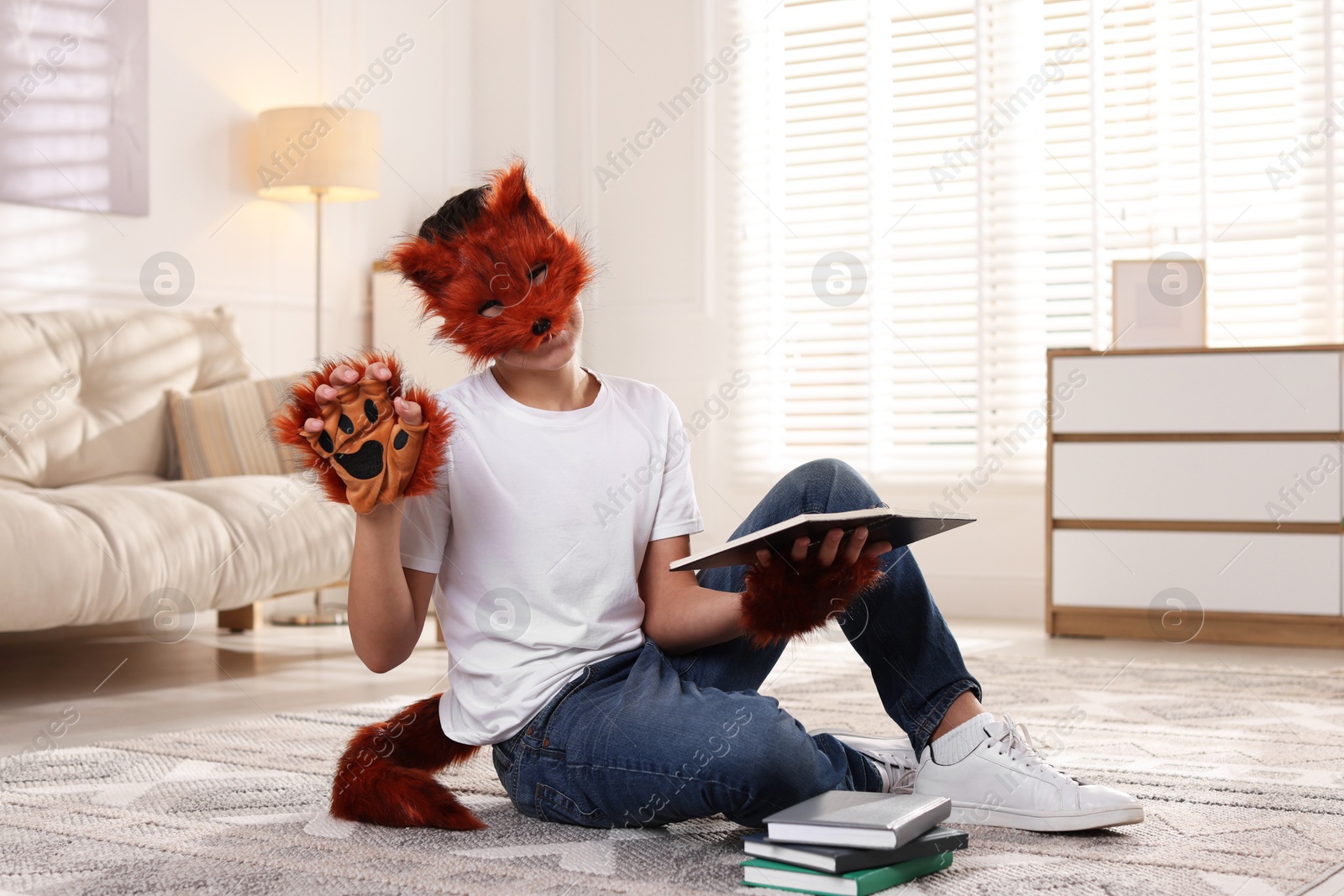 Photo of Quadrobics. Boy in fox mask, gloves and tail reading book at home