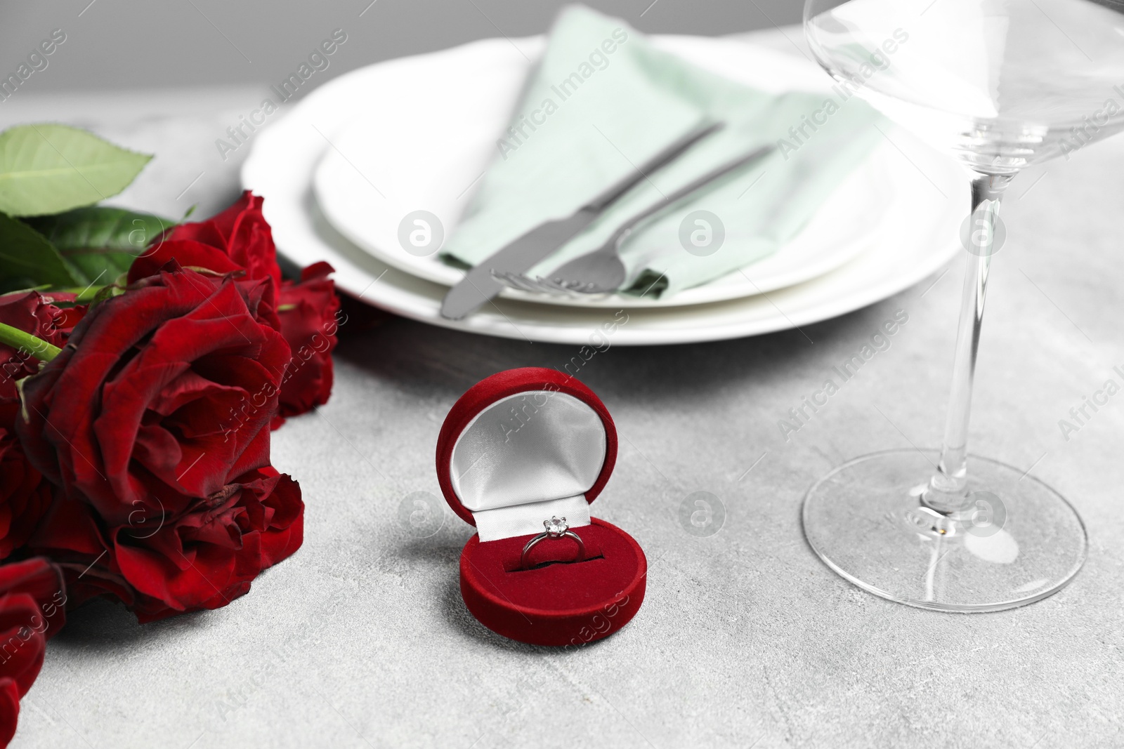 Photo of Beautiful setting for romantic dinner, engagement ring and roses on light table