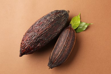 Photo of Cocoa pods and leaves on brown background, top view