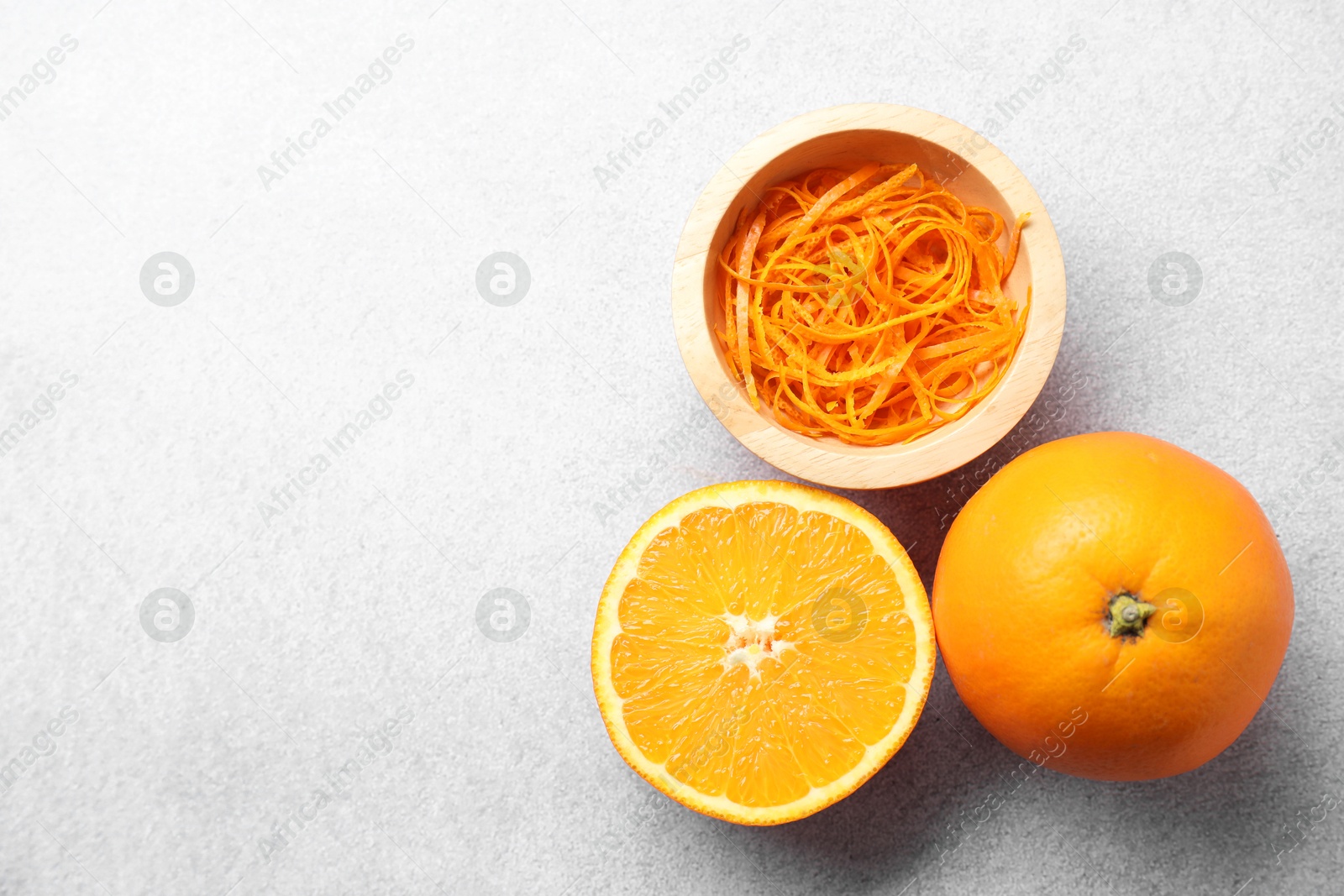 Photo of Fresh orange zest in bowl, whole and cut fruits on grey textured table, flat lay. Space for text