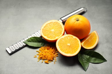 Photo of Pile of fresh orange zest, fruits, grater and leaves on grey table