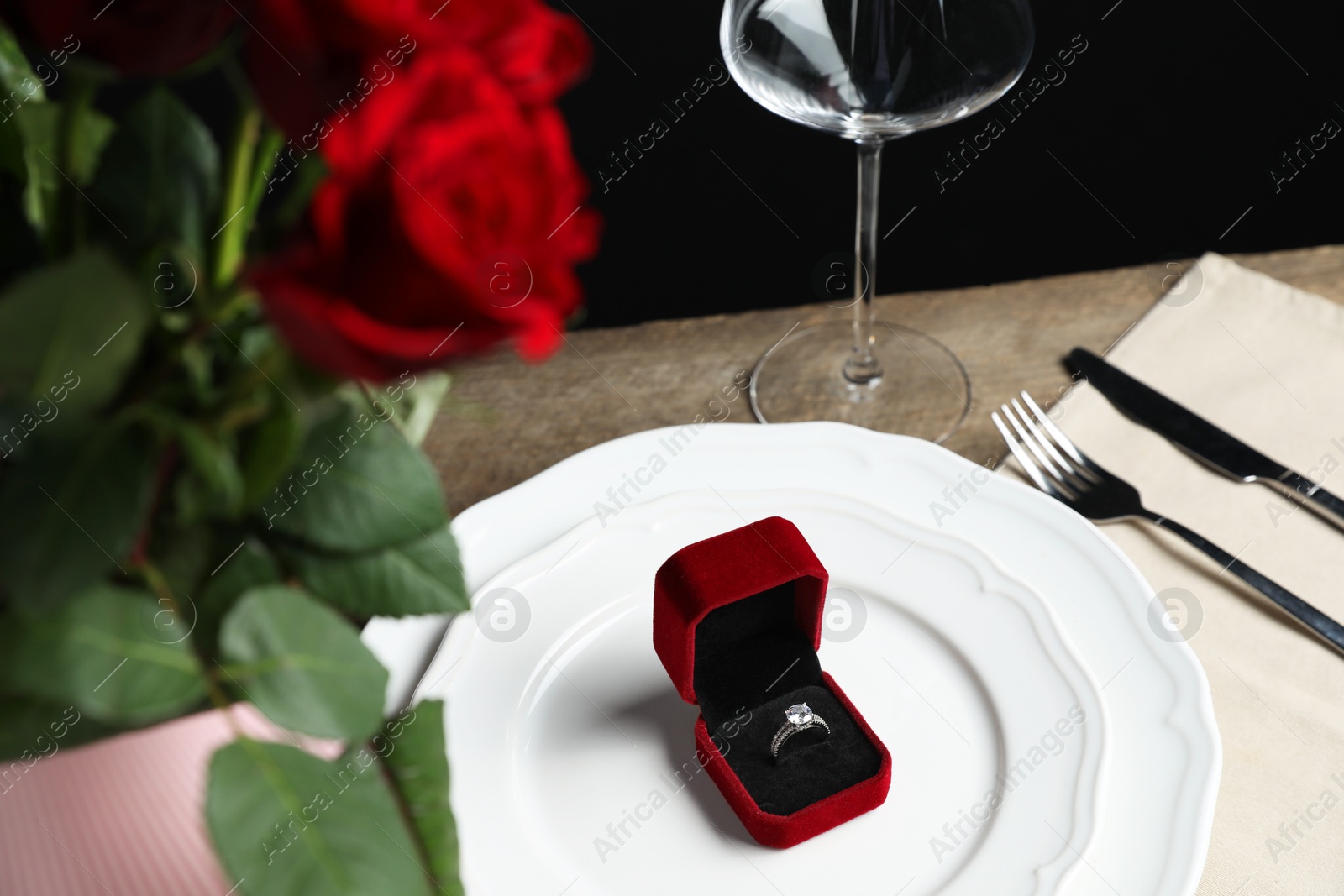 Photo of Beautiful setting for romantic dinner, engagement ring and roses on wooden table