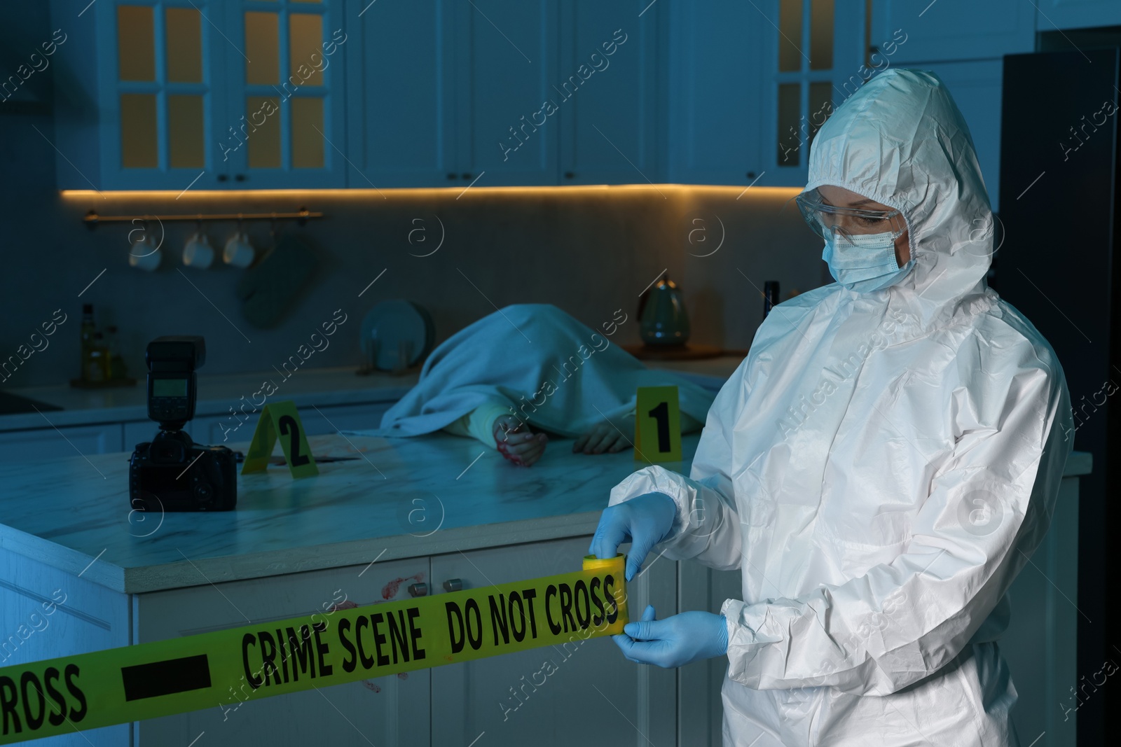 Photo of Forensic expert blocking way to crime scene and dead body with yellow tape indoors