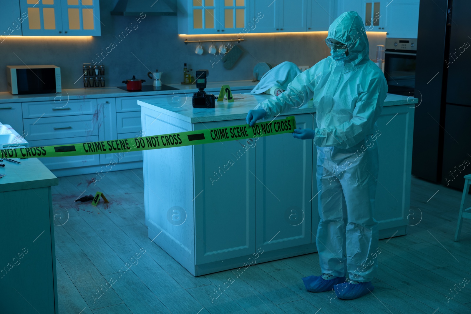 Photo of Forensic expert blocking way to crime scene with yellow tape indoors