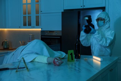 Photo of Forensic expert with camera working at crime scene and dead woman's body in dark room