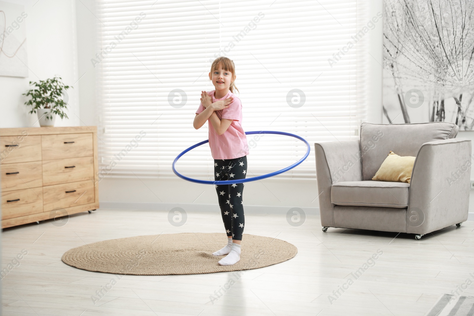 Photo of Cute little girl exercising with hula hoop at home