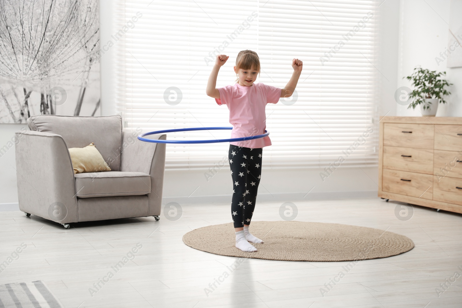 Photo of Cute little girl exercising with hula hoop at home