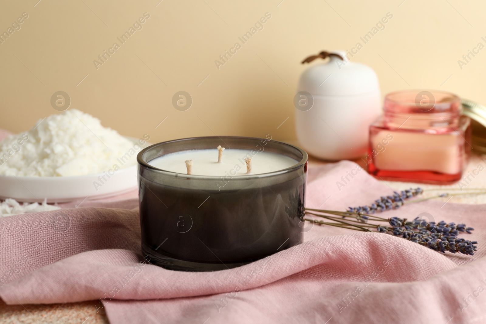 Photo of Soy wax candle, pink napkin and lavender flowers on table against beige background