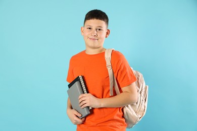 Photo of Portrait of teenage boy with books and backpack on light blue background