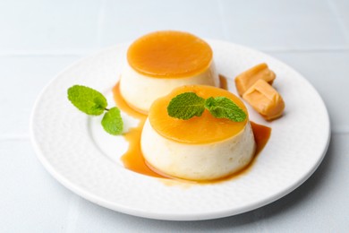 Photo of Tasty puddings with caramel sauce served on white tiled table, closeup