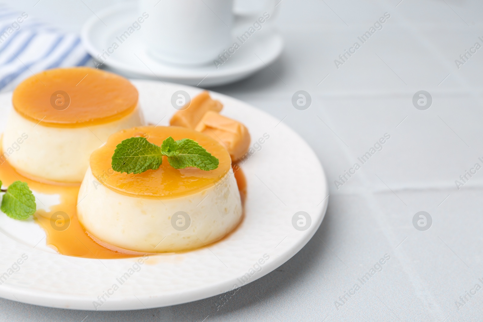 Photo of Tasty puddings with caramel sauce served on white tiled table, closeup. Space for text