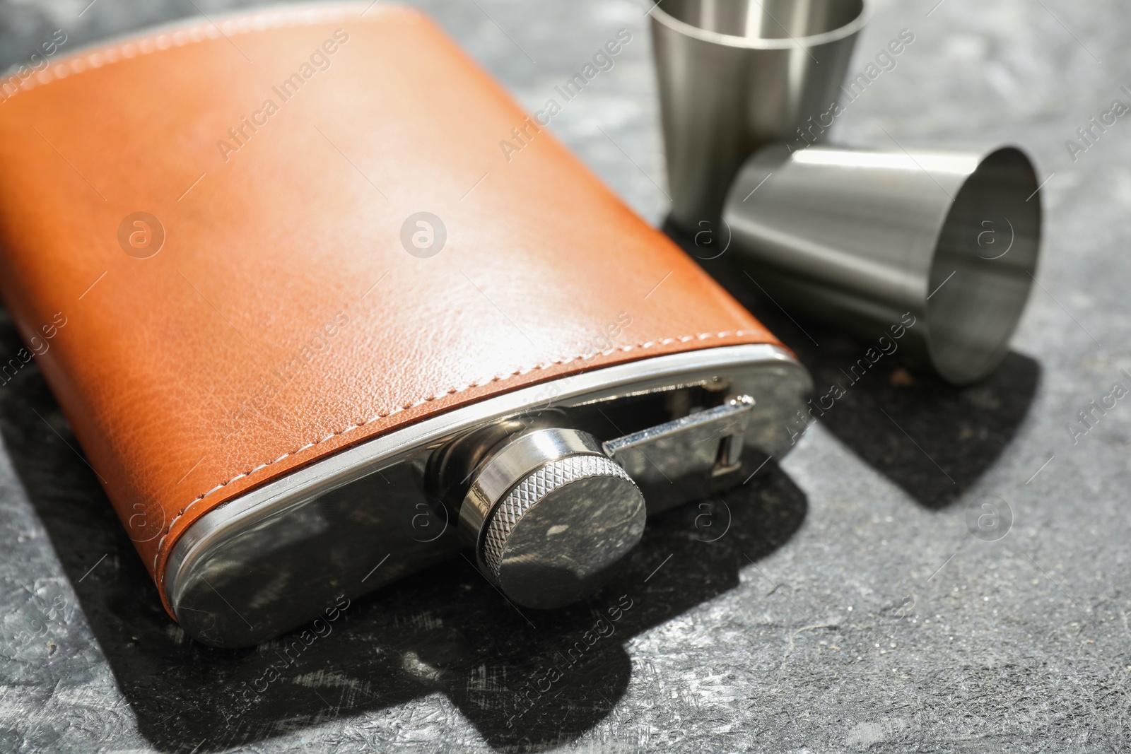 Photo of Hip flask and cups on dark table, closeup