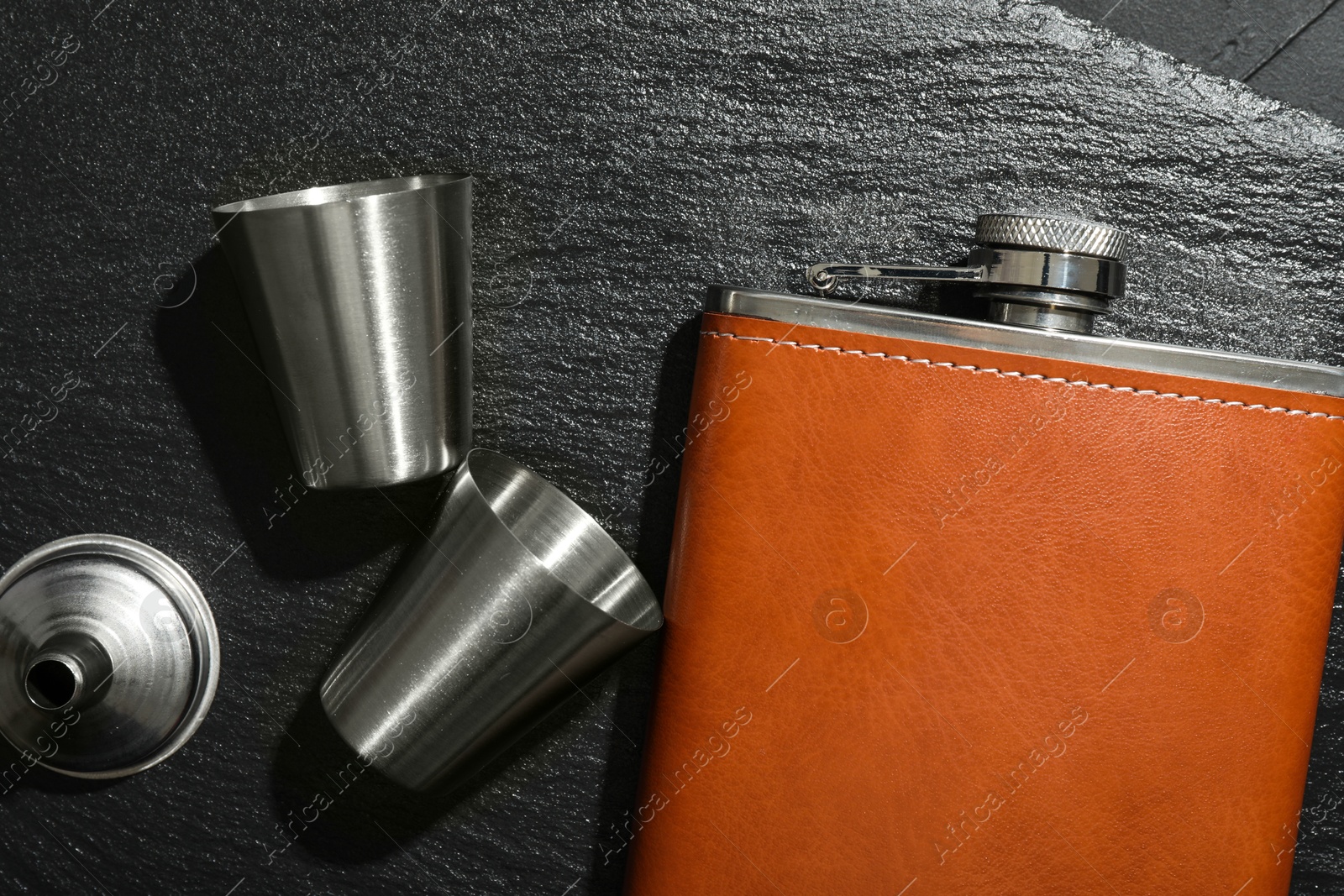 Photo of Hip flask, cups and funnel on black table, flat lay