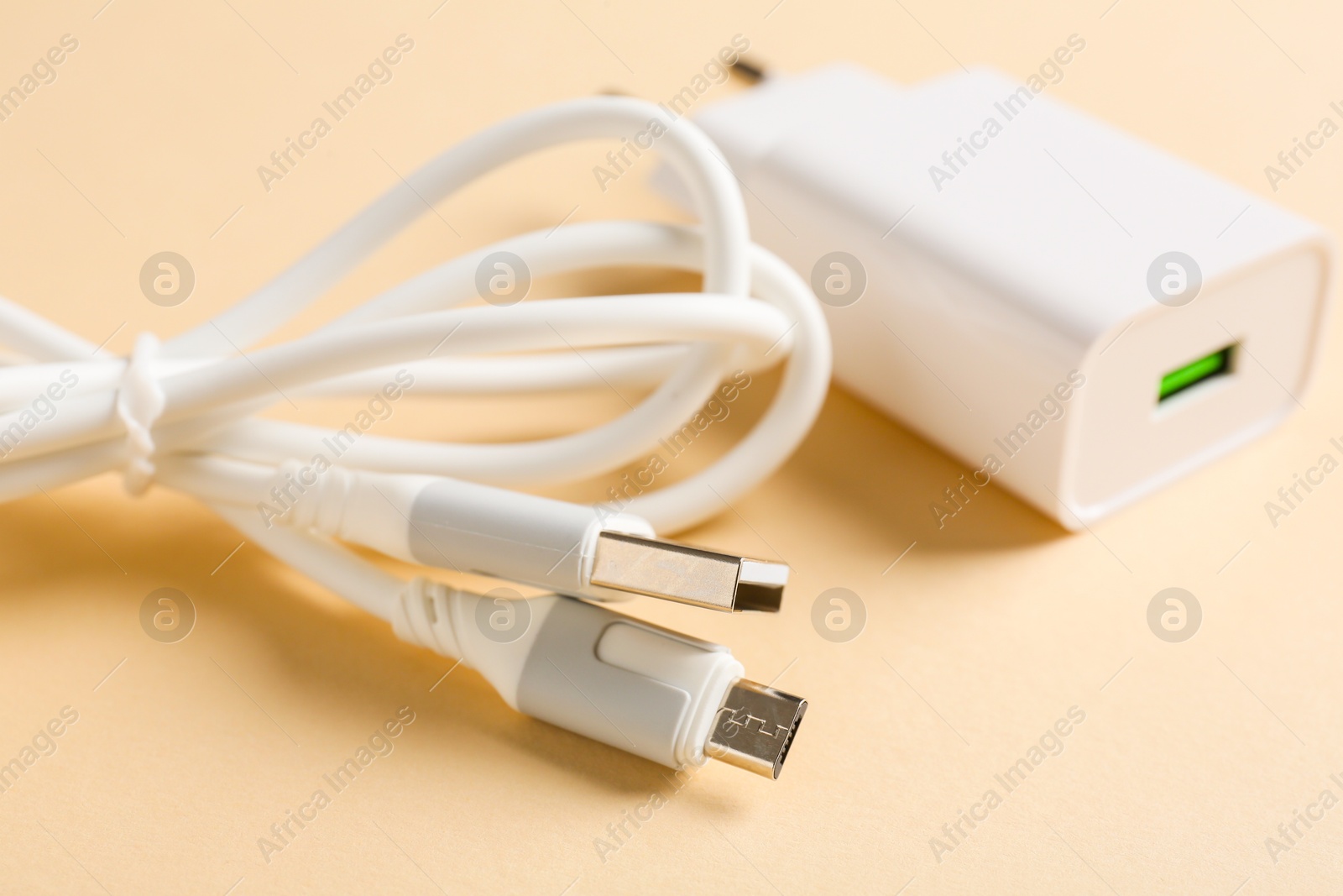 Photo of USB power adapter and charge cable on beige background, closeup