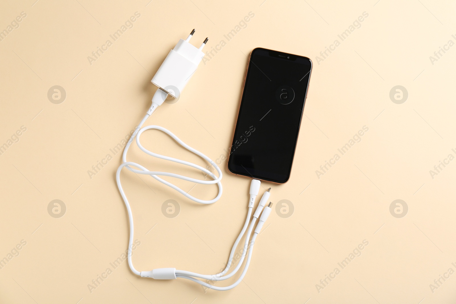 Photo of Triple charge cable connected to smartphone on beige background, top view