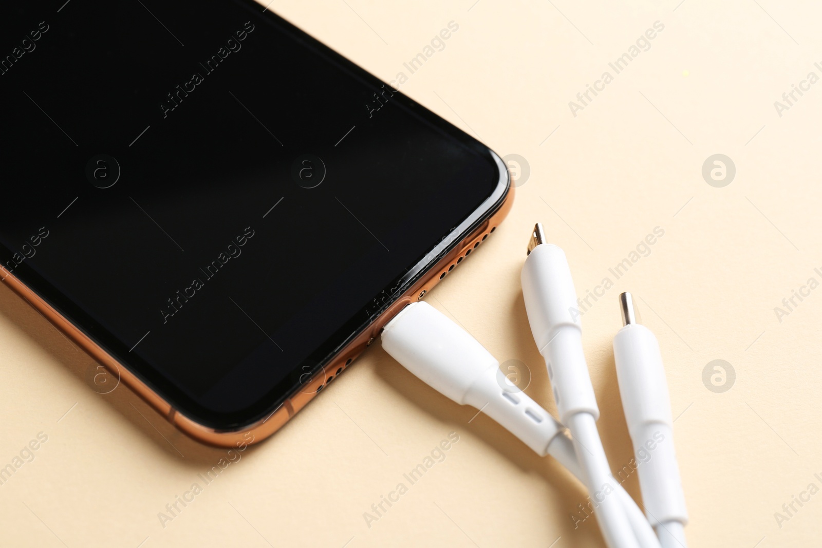 Photo of Triple charge cable connected to smartphone on beige background, closeup