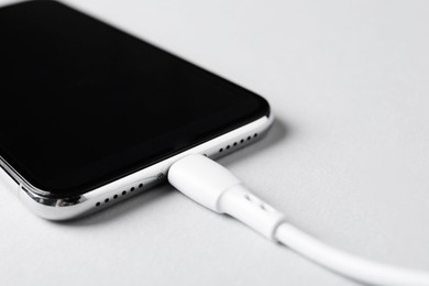 Photo of USB charge cable connected to smartphone on white background, closeup