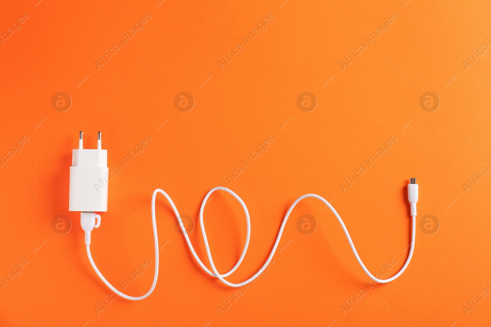 Photo of USB power adapter with charge cable on orange background, top view