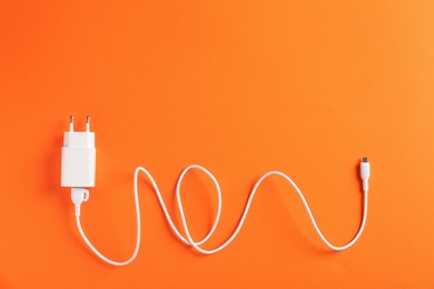 Photo of USB power adapter with charge cable on orange background, top view