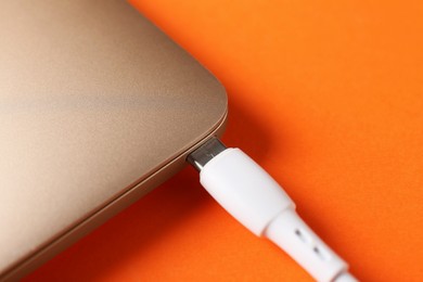 Photo of USB charge cable connected to laptop on orange background, closeup