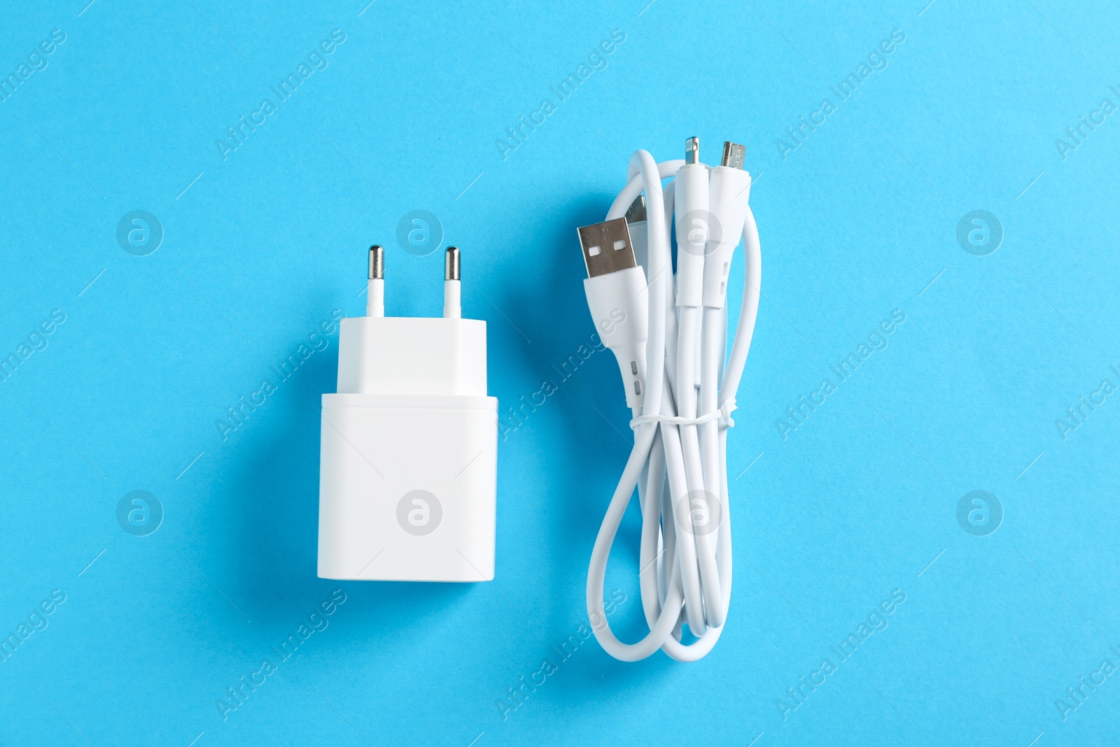 Photo of USB power adapter and triple charge cable on light blue background, flat lay