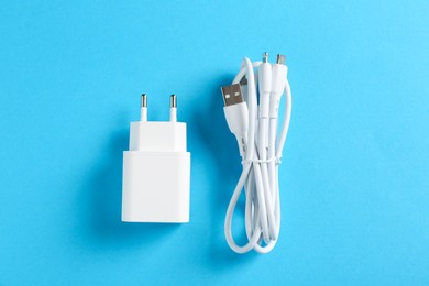 Photo of USB power adapter and triple charge cable on light blue background, flat lay