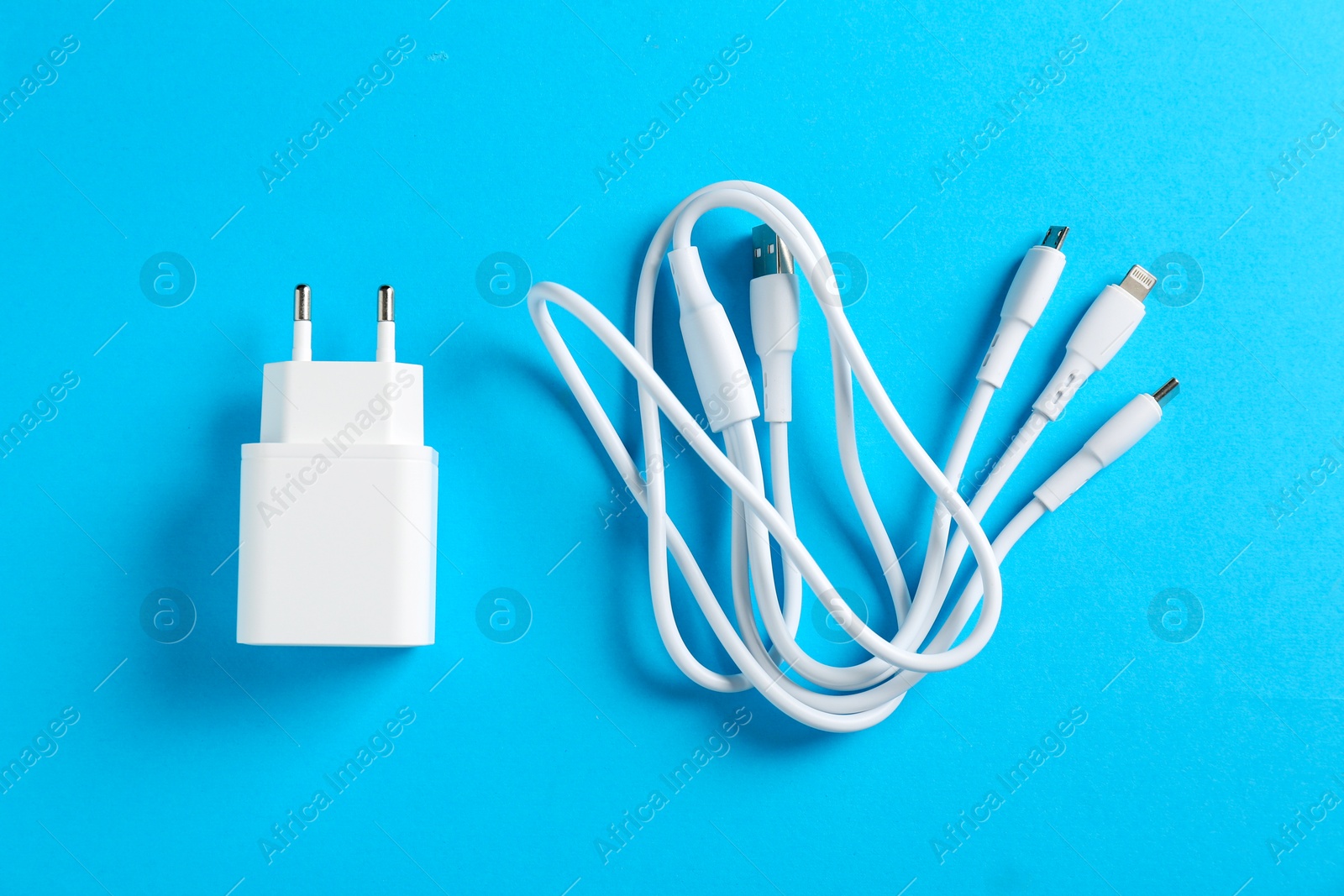 Photo of USB power adapter and triple charge cable on light blue background, flat lay