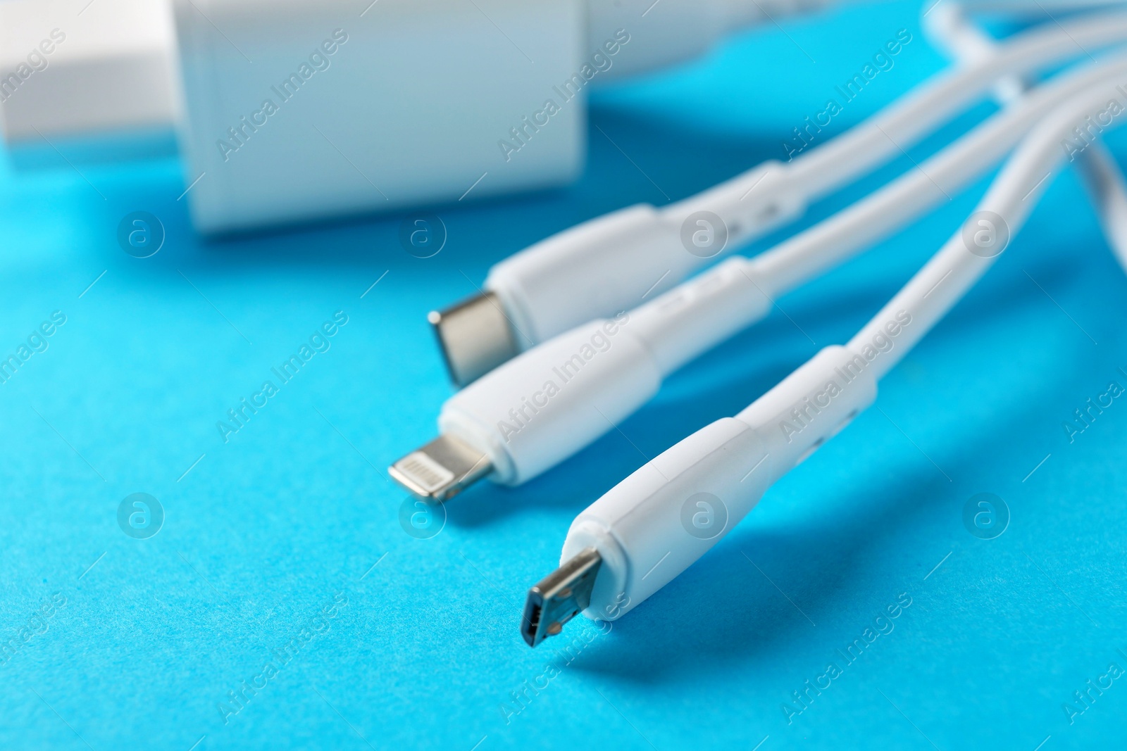 Photo of Triple charge cable and USB power adapter on light blue background, closeup. Space for text