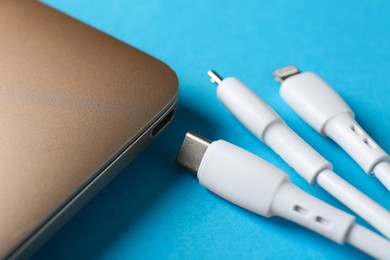 Photo of USB charge cables and laptop on light blue background, closeup