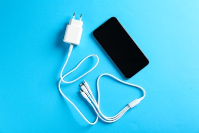 Photo of USB power adapter with charge cable and smartphone on light blue background, flat lay