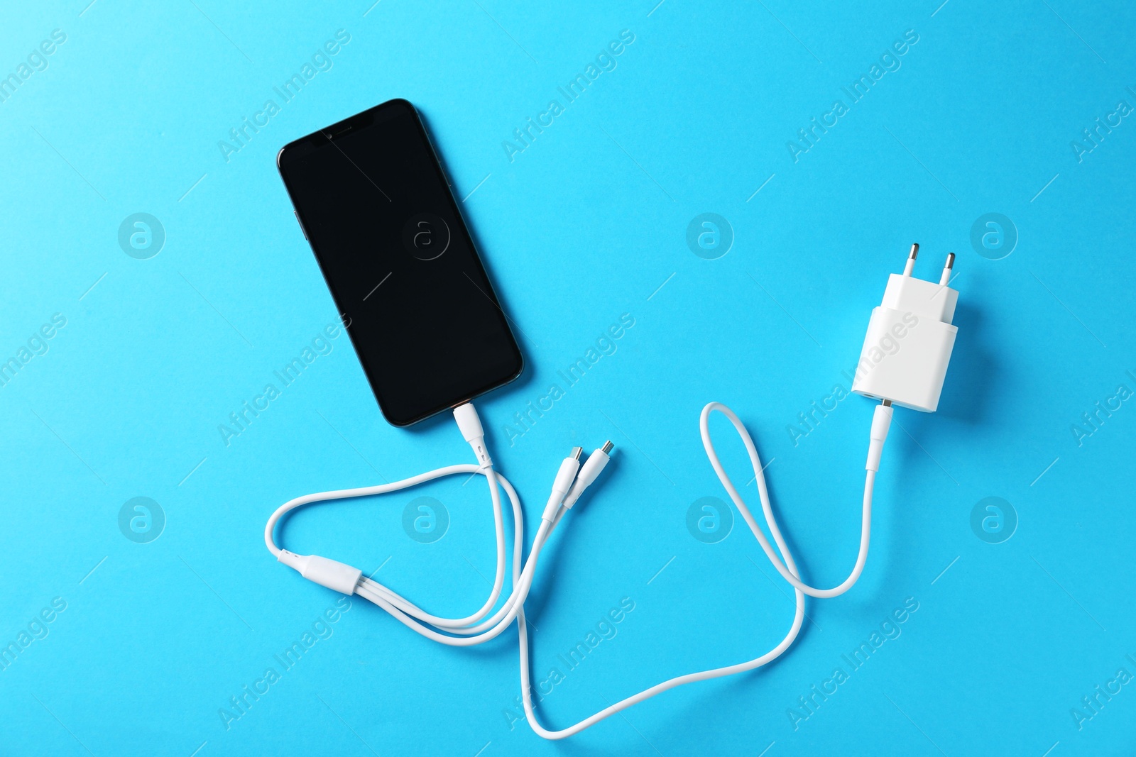 Photo of Triple charge cable connected to smartphone on light blue background, top view