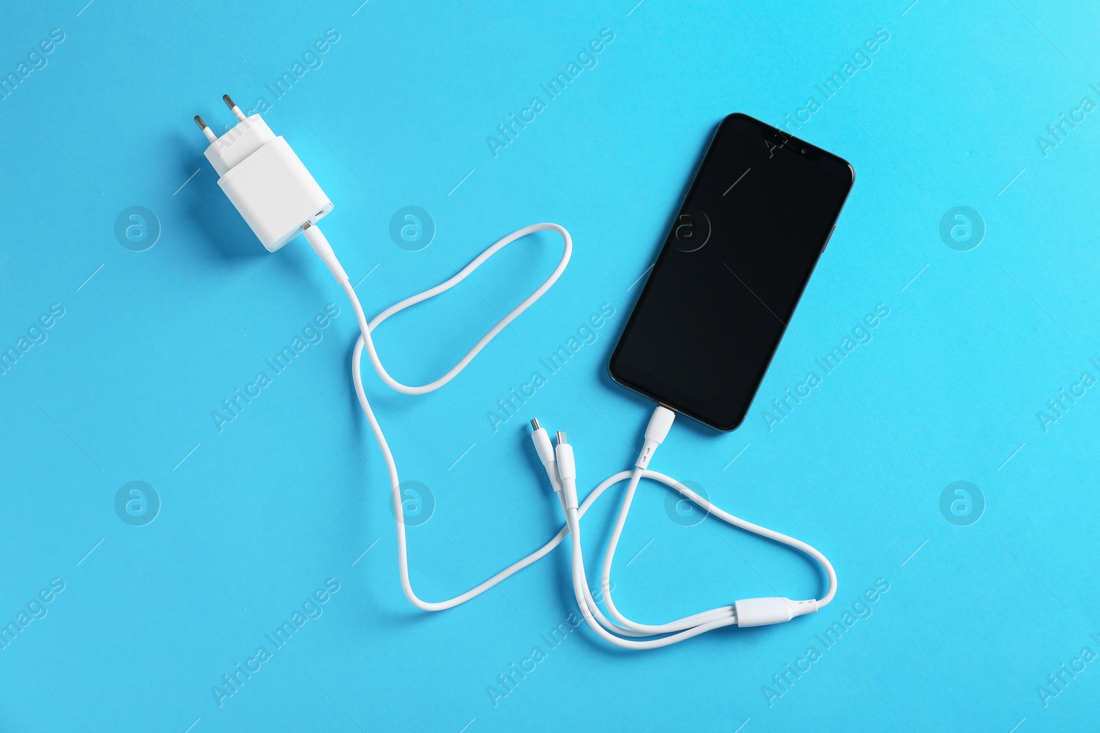 Photo of Triple charge cable connected to smartphone on light blue background, top view